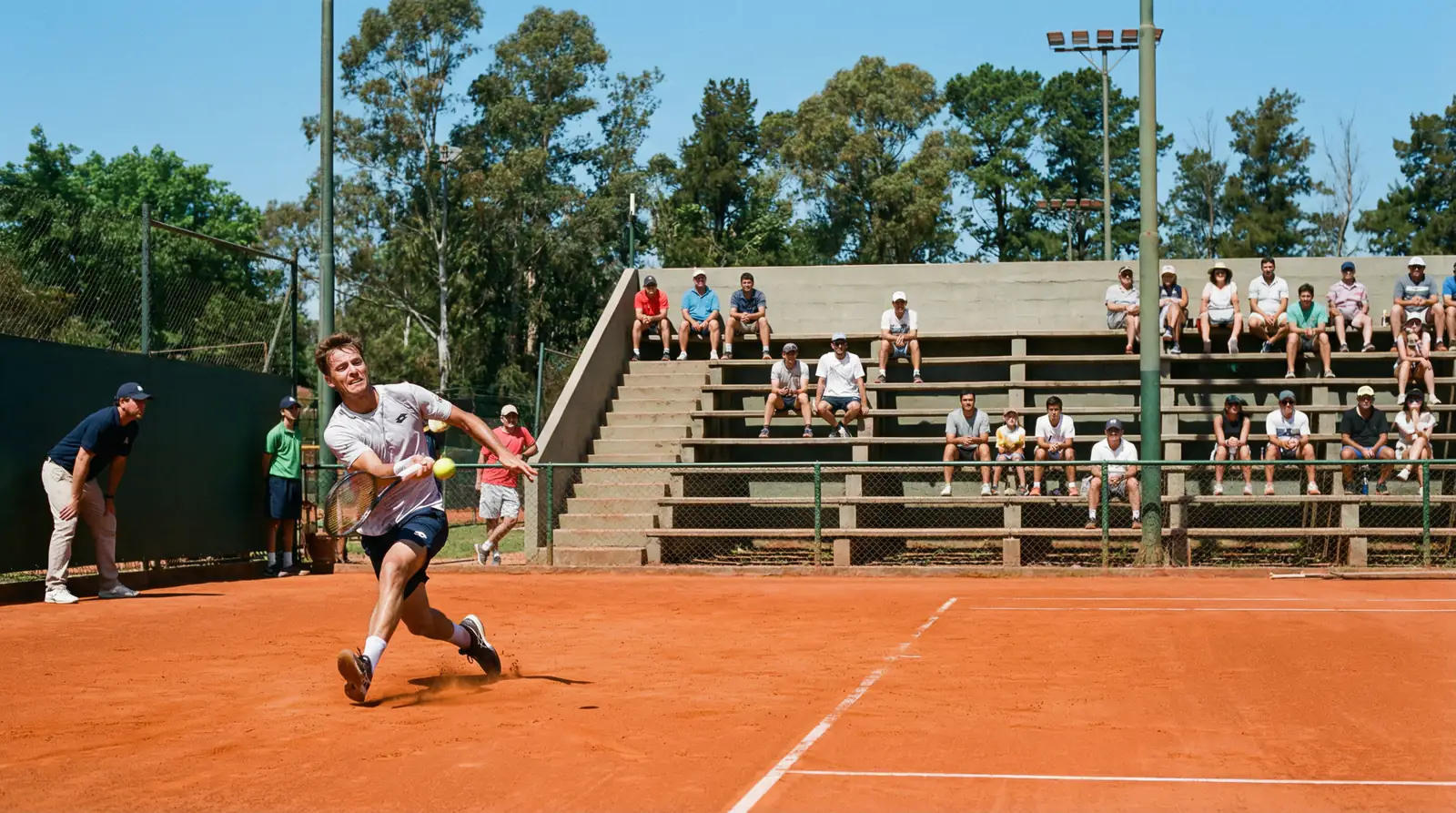 Partido de tenis en un torneo Challenger sobre tierra batida con gradas pequeñas y público cercano a la pista